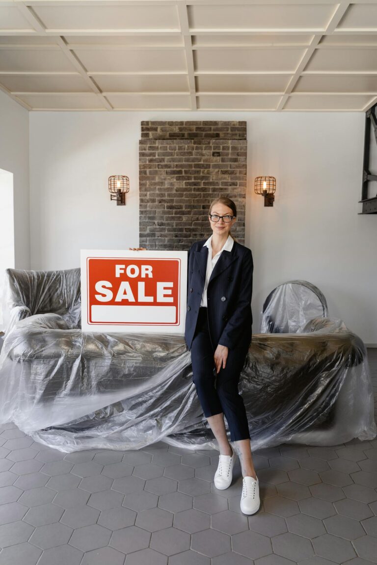 A real estate agent holding a For Sale sign in a modern living room setting.
